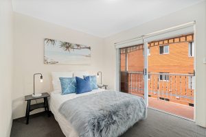 Staged bedroom with double bed, bedside tables, and sliding doors opening to a private balcony