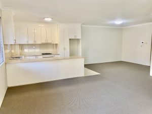 Open-plan living area with carpeted floors, adjoining kitchen, and breakfast bench at 7/39–43 Station Street, Mortdale NSW 2223