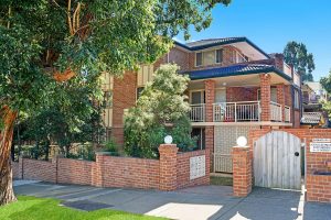 Exterior view of a red brick apartment building with balconies and landscaped frontage at 13/14–16 Cairns Street, Riverwood NSW 2210.