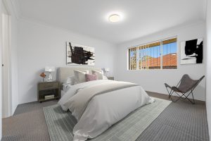 Staged bedroom with double bed, bedside tables, artwork, and window overlooking neighbouring rooftops at 13/14–16 Cairns Street, Riverwood NSW 2210.
