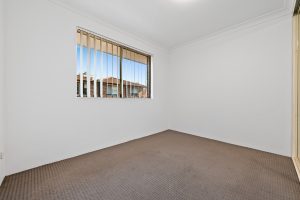 Bedroom with neutral carpet, white walls, and window with vertical blinds at 13/14–16 Cairns Street, Riverwood NSW 2210
