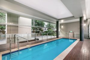 Indoor swimming pool with timber decking, glass balustrades, and full-height windows overlooking landscaped grounds at 5/1 Defries Avenue, Zetland NSW 2017
