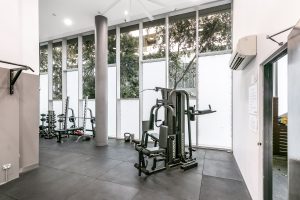 Residents’ gym with weight machines, rubber flooring, and full-height windows overlooking landscaped surroundings at 5/1 Defries Avenue, Zetland NSW 2017