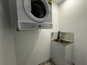 Compact internal laundry with wall-mounted washer dryer and stainless steel sink at a1208/499 Botany Road, Zetland NSW