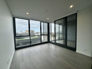 Open-plan living area with floor-to-ceiling windows, timber flooring, and corner glazing at a1208/499 Botany Road, Zetland NSW