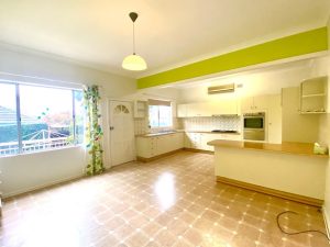Open-plan kitchen and dining area with white cabinetry, timber benchtops, built-in oven, and tiled flooring at 98 Penshurst Street, Penshurst NSW 2222
