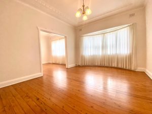 Spacious living and dining room with polished timber floors, bay window, sheer curtains, and chandelier at 98 Penshurst Street Penshurst