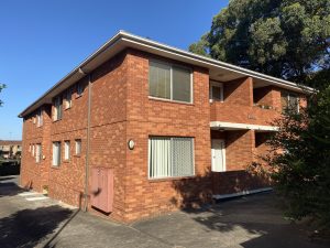 Red brick two-storey apartment building with balconies and paved driveway