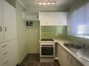 Compact kitchen with white cabinetry, electric cooktop, oven and stainless sink