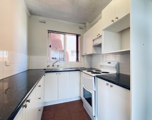 Kitchen interior with white cabinetry and black benchtops at 4/25 Romilly Street, RIVERWOOD NSW 2210
