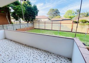 Tiled balcony overlooking shared lawn area with clotheslines and fenced yard