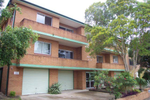Brick apartment building exterior with balconies, garage access, and landscaped frontage