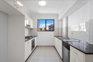 Modern galley kitchen with white cabinetry, tiled flooring, and window providing natural light at 8/13–19 Hogben Street, Kogarah NSW 2217