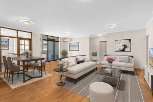 Open-plan living and dining area with timber flooring, sofas, dining table, and sliding glass doors to an outdoor space at 8/13–19 Hogben Street, Kogarah NSW 2217