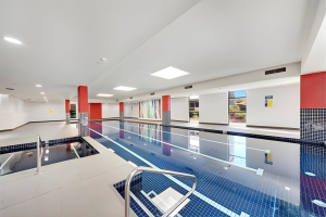Indoor lap pool with blue mosaic tiles, tiled deck, and stainless steel handrails inside a residential building at 712/12 Bonar Street, Arncliffe NSW 2205