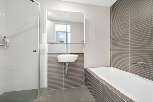 Modern bathroom with glass shower, built-in bathtub, wall-mounted basin, and neutral tiled finishes at 712/12 Bonar Street, Arncliffe NSW 2205