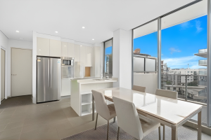 Open-plan kitchen and dining area with island bench, stainless steel appliances, and floor-to-ceiling windows at 712/12 Bonar Street, Arncliffe NSW 2205