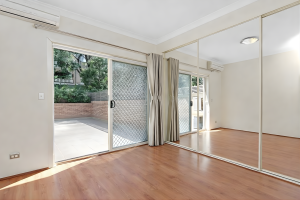 Bedroom with timber flooring, mirrored built-in wardrobes, and sliding doors to a private courtyard at 2/1–9 Andover Street, Carlton