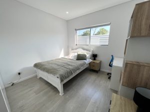 Bedroom featuring a white bed frame, study desk, shelving unit, and a window with plantation shutters.