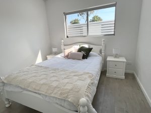 Bedroom with a white bed frame, bedside tables, and a window fitted with plantation shutters.