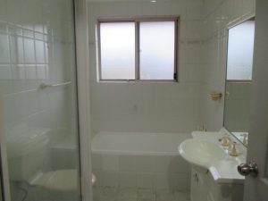 Bathroom at 10/50 Melvin Street, Beverly Hills NSW 2209 with tiled walls, bathtub, glass shower screen, vanity with basin, and frosted window