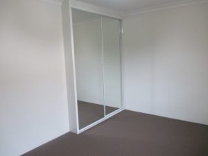 Bedroom at 10/50 Melvin Street, Beverly Hills NSW 2209 with carpet flooring, mirrored built-in wardrobe, white walls, and a simple rectangular layout