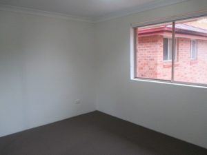 Bedroom at 10/50 Melvin Street, Beverly Hills NSW 2209 featuring carpeted flooring, neutral walls, and a window with an outlook to a neighbouring brick building
