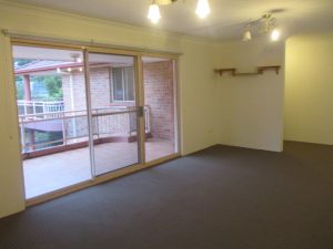 Living and dining area at 10/50 Melvin Street, Beverly Hills NSW 2209 with carpeted flooring, ceiling light fixtures, and sliding glass doors opening to a covered balcony