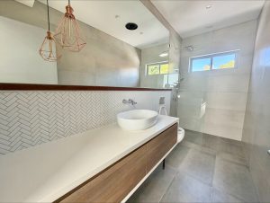 Contemporary bathroom with floating timber vanity, white vessel basin, herringbone tile splashback, frameless glass shower, and pendant lighting at 17 No