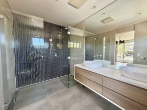 Modern bathroom with glass walk-in shower, black herringbone tile wall, floating timber vanity, twin vessel sinks, and large wall mirror at 17 Northbrook St, Bexley NSW 2207