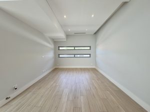 Modern interior room with timber-look flooring at 17 Northbrook Street Bexley NSW 2207, showing a long rectangular layout, light timber-look floor tiles, recessed ceiling lighting, high ceilings, and narrow horizontal windows along the far wall.