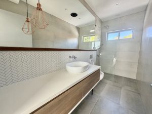 Modern bathroom with double vanity and glass shower at 164 Queen Victoria Street Bexley NSW 2207, showing a long floating timber vanity, twin vessel basins, herringbone tiled splashback, pendant lights, and a frameless glass shower with tiled flooring.